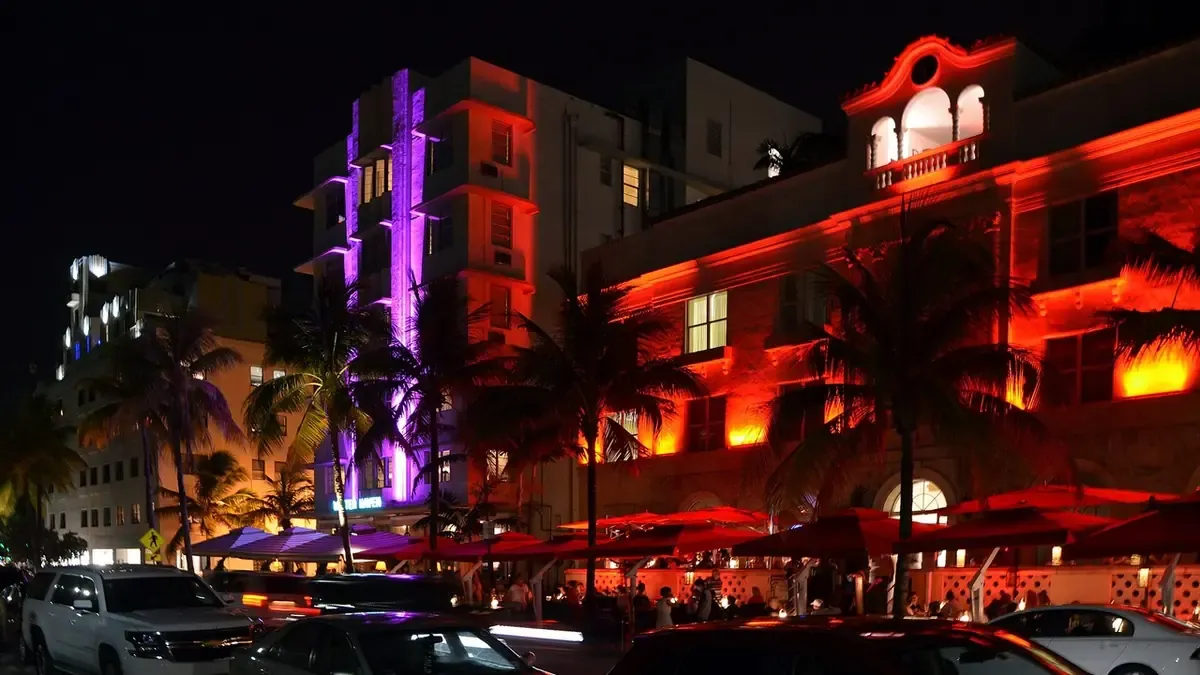 Foto real de Ocean Drive, en Miami Beach, de noche: hoteles art déco con luces de neón rojas y moradas